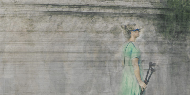 a woman wears a green dress and crutches and walks on bridge ponte vittorio emanuele ii in rome